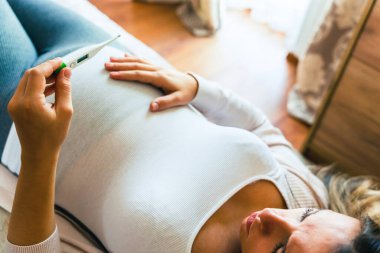 Hamilelik ateşi kontrolü. Hamile kadın termometre tutuyor, ateşi kontrol et. Hamile kız hasta. Hamilelik kavramı, annelik, bebek doğumu beklentisi