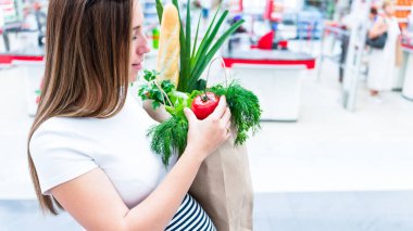 Kadın süpermarket yiyecek çantası. Hamile bir anne sağlıklı sebzelerle, marketteki marketin arka planında taze marul salatası yapraklarıyla. Günlük alışveriş konsepti