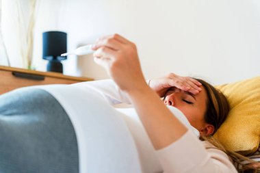 Hamilelik ateşi kontrolü. Hamile kadın termometre tutuyor, ateşi kontrol et. Hamile kız hasta. Hamilelik kavramı, annelik, bebek doğumu beklentisi