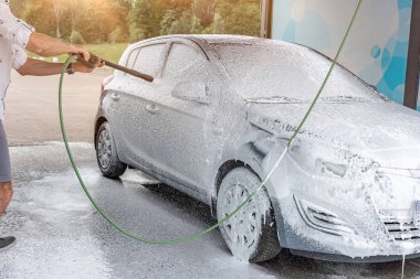 Araba temizliği. Adam arabayı spreyle yıkıyor. Köpüklü su sabunu servisi.