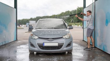 Adam arabayı temizliyor. Sprey hortum köpük sabunu. Araba yıkama suyu dış görünüşü parlatır.