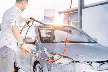 Adam arabayı temizliyor. Sprey hortum köpük sabunu. Araba yıkama suyu dış görünüşü parlatır.