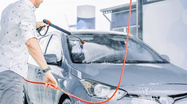 Araba temizliği. Adam arabayı spreyle yıkıyor. Köpüklü su sabunu servisi.