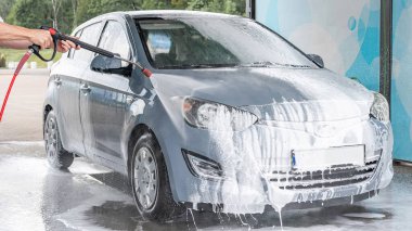 Adam arabayı temizliyor. Sprey hortum köpük sabunu. Araba yıkama suyu dış görünüşü parlatır.