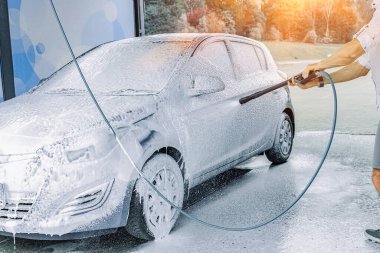 Adam arabayı temizliyor. Sprey hortum köpük sabunu. Araba yıkama suyu dış görünüşü parlatır.