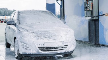 Adam arabayı temizliyor. Sprey hortum köpük sabunu. Araba yıkama suyu dış görünüşü parlatır.