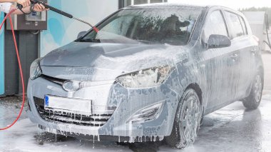 Adam arabayı temizliyor. Sprey hortum köpük sabunu. Araba yıkama suyu dış görünüşü parlatır.