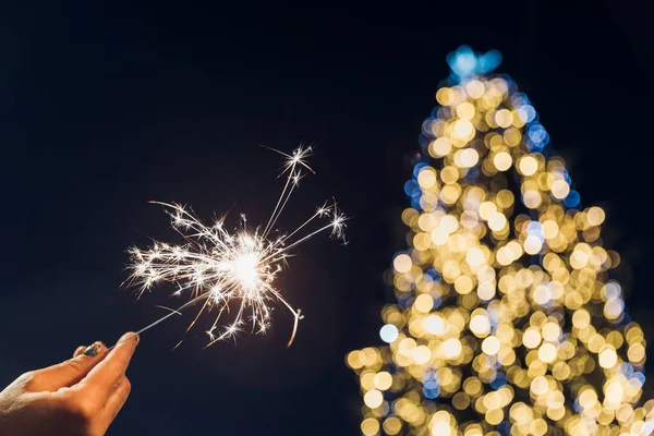 手里拿着一个火花 一棵有节日彩灯的圣诞树 圣诞及新年庆祝活动 — 图库照片