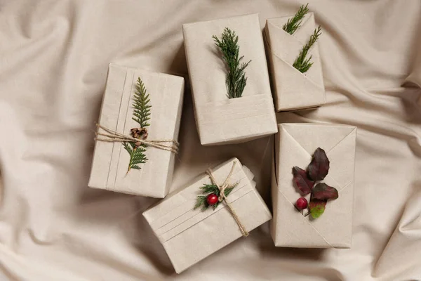 四个圣诞礼品盒 时尚和服风格与环保材料 亚麻纺织品背景上有褶皱 天然枝条和浆果的牛皮纸 — 图库照片