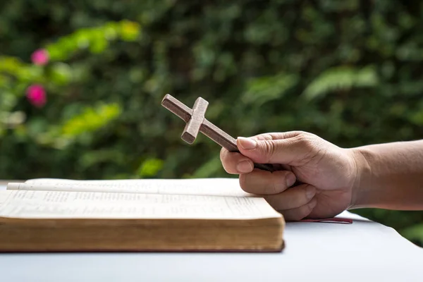 Man holding a wooden religious cross crucifix with an open bible. Christian faith concept.