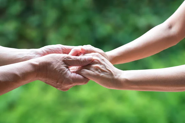 stock image Two people holding hand together, with green nature background. Helping hand or emotional support concept.