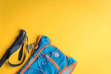 Hiking stick and backpack on yellow background. Hiking or mountain climbing concept. Top view.