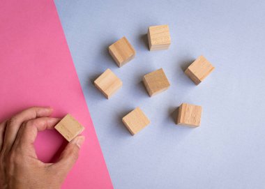 Wooden blocks on blue and pink background with a hand picking one of the blocks. Leadership, human resources, team or hiring concept.