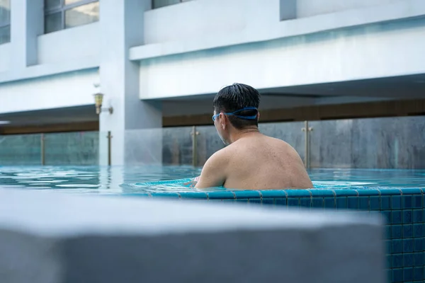 Back view of man in the pool, relaxing by the side. Vacation or travel concept.