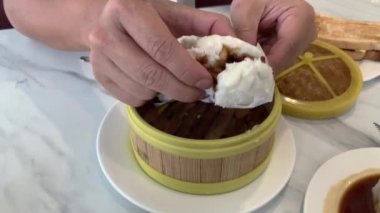 Adam yeni pişmiş bir Hong Kong Dim Sum tarzı char siew pork (ağır ateşte pişirilmiş et) böreği açtı, yemeye hazır. Çin / Hong Kong tarzı restoranda kahvaltı.