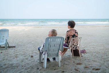Yaşlı çift sahilde dinleniyor, denizi izliyorlar. Yaşlılar ve emekliler için tatil ve tatil kavramı.