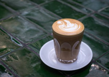 Yeşil fayansların üzerinde camdan yapılmış bir fincanda sade beyaz kahve. Boşluğu kopyala.