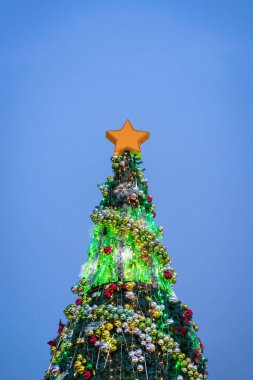 Güzel dekore edilmiş Noel ağacı, akşam mavisi gökyüzü arkaplanıyla aydınlandı. Boşluğu kopyala.
