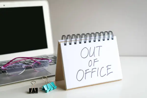 Out of office, message next to computer laptop. On office desk.