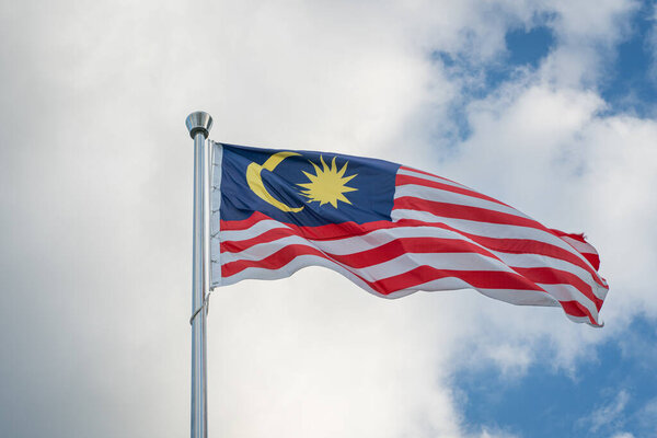 Malaysia flag tied to a pole waving against the blue sky and clouds.