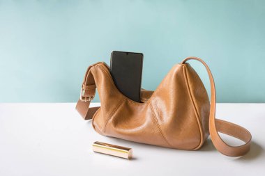 Telefonlu ve rujlu bir kadın çantası. Beyaz tablo ve mavi arkaplan, boşluğu kopyala.