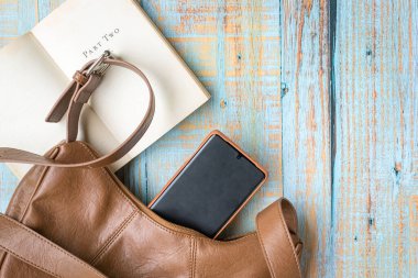Kahverengi deri kadın çantası, telefon ve karton kaplı kitap. Üst görünüm, alanı kopyala.