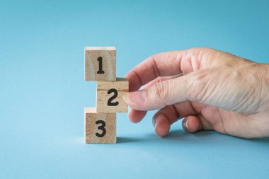 Kadın eli, üzerinde 123 numara olan 3 tahta küpü dikey olarak ayarlıyor..