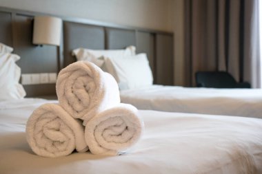 Yatağın üstünde rulo beyaz havlular olan çağdaş bir otel odası..