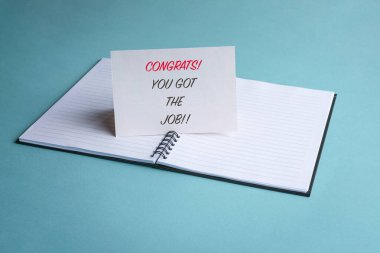 Congrats you got the job, a message on a white card on top of a notepad. New job or employment concept. clipart