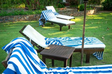 Deckchairs with large blue stripes bath towel. Holiday or vacation concept. clipart