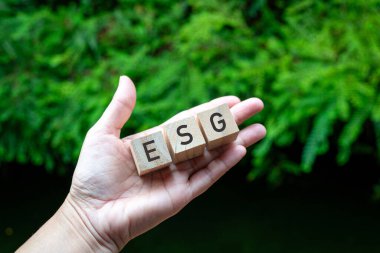 Kalem avuç içinde üç oyuncak bloklu ESG kelimesi. Yeşil doğa arkaplanı.