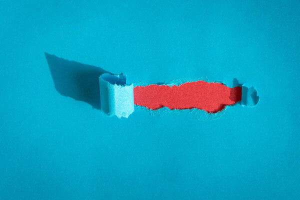 Дыра разорвана синей бумагой на красном фоне. Копирование пространства
.