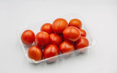 Küçük vişneli lezzetli kırmızı domatesler plastik pakette, beyaza yakın.
