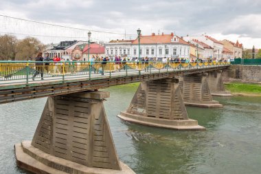 Uzhhorod, Ukrayna - 19 Nisan 2023: İnsanlar şehir merkezindeki Uzh Nehri üzerindeki yaya köprüsünde yürüyor. Ukrayna 'nın batısında, Slovakya sınırında bir şehir ve belediyedir..