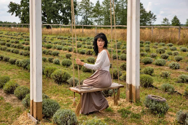 stock image Beautiful young brunette caucasian woman sitting on a wooden swing against the lavender field closeup.