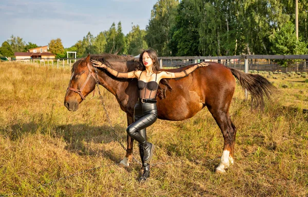 美丽的年轻黑发女人穿着黑色皮衣站在马旁边 — 图库照片