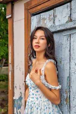 Yazlık elbiseli güzel beyaz kadın kırık boyalı eski kapının önünde duruyor, yakın plan..