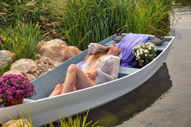 Güzel, genç, esmer, beyaz bir kadın. Tahta bir teknede yatıyor. Yakın plan..