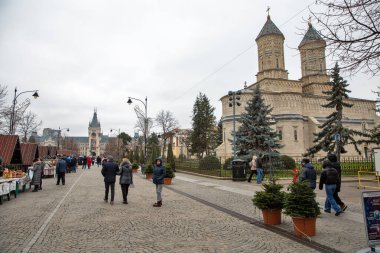 Iasi, Romanya - 26 Aralık 2024: İnsanlar Büyük Stephen ve Aziz Bulvarı 'ndaki Noel Fuarı' nı ziyaret ediyorlar. Kutsal Üç Hiyerarşik Manastırı sağda görünüyor..