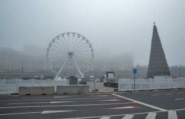 Bükreş, Romanya - 31 Aralık 2024: Anayasa Meydanı 'nda kış aylarında yoğun sis varken, Noel ağacı ve Parlamento Sarayı önünde dönme dolap kapalı..