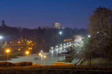 View from National Heroes Memorial over night Carol Park with lake and Palace of Parliament in the background. Bucharest, Romania.