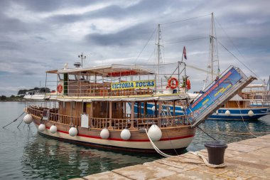 Porec, Hırvatistan - 21 Mayıs 2025: Geleneksel tahta tekne Victoria Tours marinaya yanaştı. Tekne Rovinj 'e günlük geziler, yunus gözlemleri ve bulutlu gökyüzünün altında Lim Fjord sunuyor..