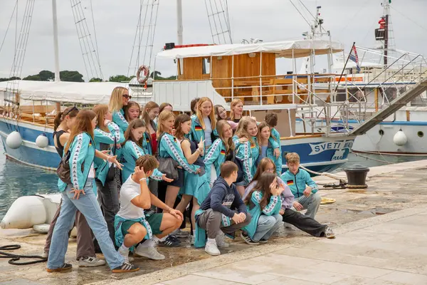 Porec, Hırvatistan - 21 Mayıs 2025: Neşeli bir gençlik grubu Sveti Marko adlı gemi yakınlarında çekilen bir grup fotoğrafı için poz veriyor. Eşleşen ceketler giyerek eğitim, spor ya da eğlence amaçlı bir gezide gibi görünüyorlar..