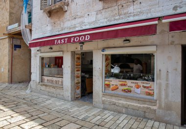 Porec, Hırvatistan - 21 Mayıs 2025: Eski bir Avrupa kentinde küçük bir fast food restoranının sokak manzarası. Taş bina cephesi, penceredeki menü posterleri, kaldırım taşı caddesi, günlük yemek, yerel yemek sahnesi..