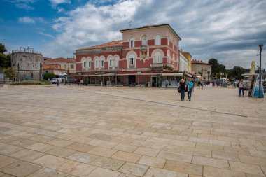 Porec, Hırvatistan - 21 Mayıs 2025: Turistler tarihi renkli binalar ve ortaçağ taş kulesiyle Eski kasaba meydanında yürüyorlar. Kafeleri ve restoranları olan popüler bir turizm bölgesi..