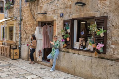 Porec, Hırvatistan - 21 Mayıs 2025: Küçük bir butiğin önünde dikilen iki genç kadın, Old Town 'da büyüleyici bir kaldırım caddesinde giysi ve el yapımı aksesuarlar satıyor.