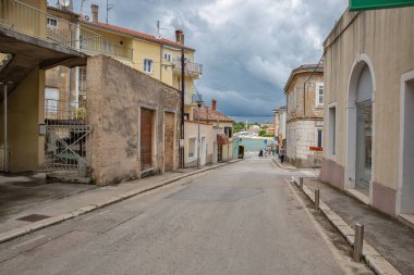 Porec, Hırvatistan - 21 Mayıs 2025: Geleneksel İstriya taş binaları, yıpranmış cepheleri, terasotta çatıları Adriyatik Denizi limanına doğru uzanan bulutlu gökyüzü altında uzanan eski kentteki eğim caddesi.