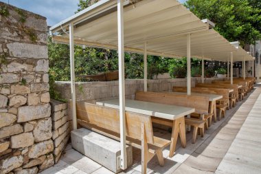 Hırvatistan 'ın Porec kentindeki açık hava kafe terasında, taş yol boyunca sıralanmış uzun ahşap banklar ve masalar dinlenmek veya yemek yemek için sakin ve güneşli bir yer sunuyor.