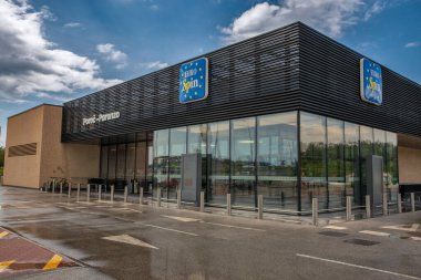 Porec, Hırvatistan - 21 Mayıs 2025: Pürüzsüz cam duvarlar ve yağmurdan sonra kara panele sahip modern Eurospin süpermarketi, gökyüzünü ve kentsel çevreyi yansıtıyor.