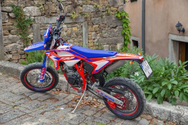 Motovun, Hırvatistan - 22 Mayıs 2025: Liqui Moly amblemli mavi ve kırmızı KTM arazi motosikleti, tarihi kaldırım taşı caddesinde park edilmiş tarihi taş duvara karşı ortaçağ kenti Istria 'da.